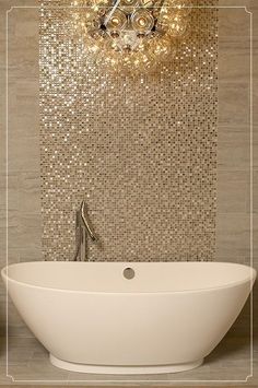 a white bath tub sitting under a chandelier next to a wall mounted mirror