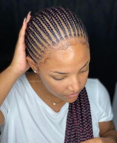 a woman with cornrows is looking down at her cell phone while wearing a white t - shirt