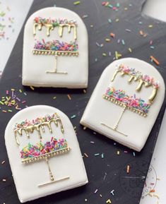 three decorated birthday cakes sitting on top of a black tray covered in sprinkles