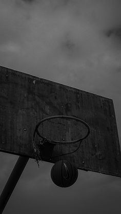 an old basketball hoop with a basket in the air against a cloudy sky and dark clouds