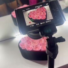 a camera is on top of a tripod with pink roses in the shape of a heart