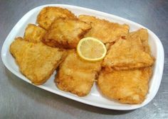 fried fish with lemon wedges on a white platter sitting on a metal table