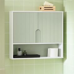 a bathroom with green tiled walls and white cupboards above the toilet paper dispenser