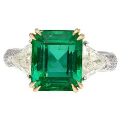 An individualistic statement of love, this three stone engagement ring showcases a natural Brazilian 5.31-carat no oil emerald. The emerald is AGL certified. Additionally, the ring boasts two triangular (trillion) cut white diamonds on each side of the emerald, totaling 1.10 carats and measuring 6 mm each, and 28 round-cut white diamonds, totaling 0.38 carats and measuring 1.5 mm each. Crafted with a platinum 900 shank and 18k gold, this ring is a testament of blended beauty and a perfect beginning to a new romance. About the emerald: This gem achieves the a vibrant, dense green color saturation with excellent luster, clarity, and superb transparency. Extremely rare considering the emerald has no oil treatment of any kind. Featuring a South American Brazil origin. Item Details: - Type: Eng Trillion Diamonds, 3 Stone Ring, 3 Stone Rings, Three Stone Engagement, Three Stone Engagement Rings, Platinum Ring, Emerald Jewelry, Three Stone Rings, Yellow Diamond