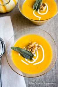 two bowls filled with soup on top of a table next to silverware and pumpkins