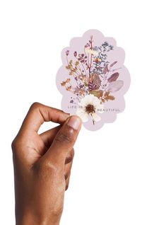 a hand holding up a sticker with flowers on it's side and the words life is beautiful