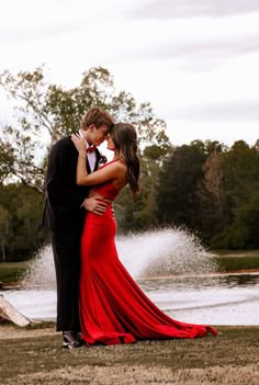 a man and woman standing next to each other in front of a lake