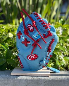 a blue baseball glove sitting on top of a wooden base in front of some plants