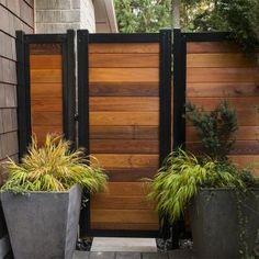 two large planters sitting next to each other in front of a wooden fence and gate