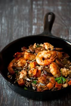 a skillet filled with shrimp and rice on top of a wooden table next to a fork