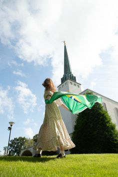 a woman holding a green kite in front of a white building with a steeple