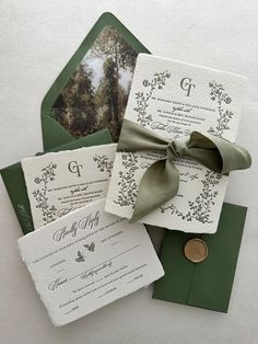 the wedding stationery is laid out on top of green envelopes, with a ribbon tied around it