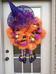 a purple and orange halloween wreath hanging on the front door with witch legs in it