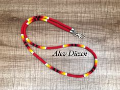 a red, yellow and black beaded dog leash on a wooden surface with the word aeo dizen