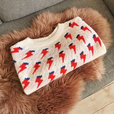 a white sweater with red and blue lightnings on it sitting on a fur rug