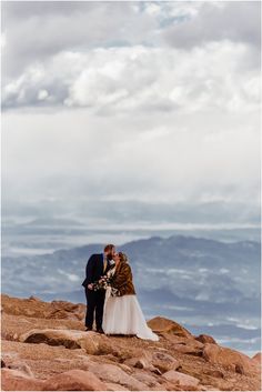 a bride and groom kissing on top of a mountain