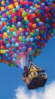 there is a large group of balloons flying in the sky above a house and clouds