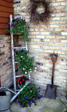 an old ladder with flowers growing on it next to a brick wall and garden tools