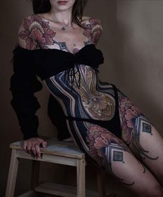 a woman with tattoos on her body sitting on a stool