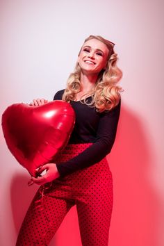 a woman holding a heart shaped balloon in her right hand and smiling at the camera