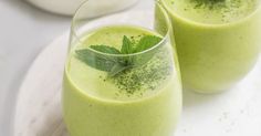 two glasses filled with green smoothie on top of a white plate