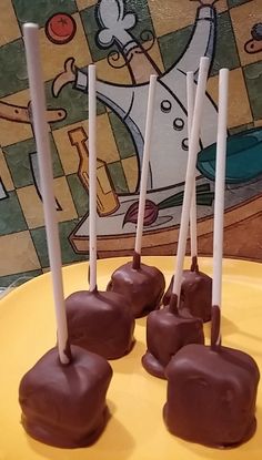 four chocolate covered candy lollipops sitting on a yellow plate with white sticks