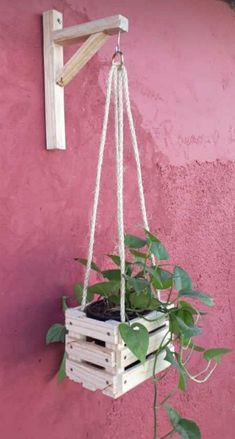 a hanging planter made out of wooden pallets with plants growing in it on the side of a pink wall