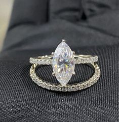 a white diamond ring sitting on top of a black cloth covered seat next to a pillow