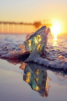 the sun is setting behind an iceberg in the water with its reflection on it