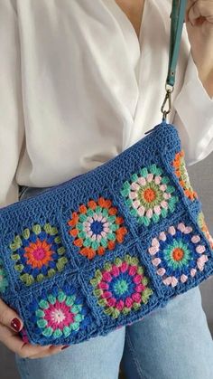 a woman holding a blue crocheted purse with flowers on the front and sides