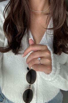 a woman wearing a white sweater and black sunglasses with her hands folded over her chest