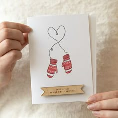 a person holding up a card with mittens on it and a heart hanging from the string