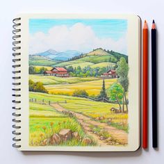 an open notebook with colored pencils next to it and a drawing of a rural landscape