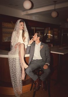 a man sitting next to a woman on top of a chair in front of a bar