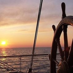 the sun is setting over the ocean as seen from a ship's steering wheel