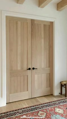 two wooden doors in a room with a rug on the floor and a table next to it