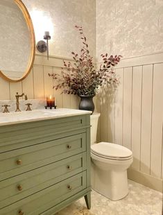 a white toilet sitting next to a green dresser in a bathroom under a round mirror