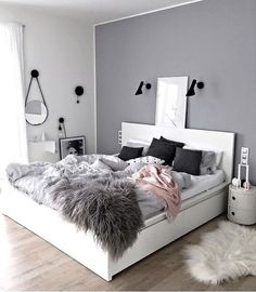 a white bed sitting in a bedroom next to a window with lots of pillows on top of it