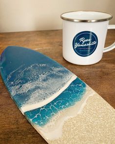 a surfboard sitting on top of a wooden table next to a cup