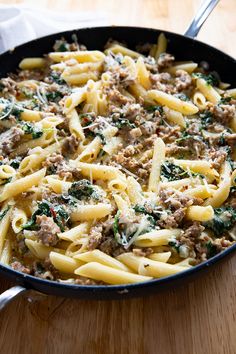 a skillet filled with pasta, meat and spinach on top of a wooden table