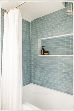 a white shower curtain in a blue tiled bathroom with tub and shelf on the wall