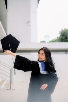 a woman in graduation gown holding up a black hat