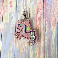 a keychain with a pink unicorn on it sitting on top of a wooden surface