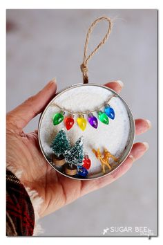 a hand holding a glass ornament with christmas lights and ornaments on it's side