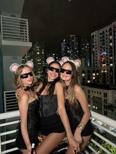 three women in black cats ears posing for a photo on top of a building at night