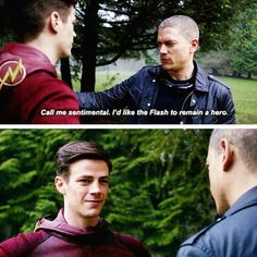 the flash and arrow are talking to each other in front of some trees, one is wearing