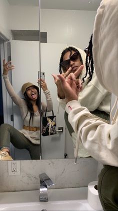 a woman taking a selfie in front of a bathroom mirror with her hand up