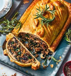 a meat pie on a platter with rosemary sprigs and other toppings