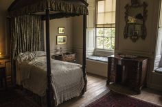 a bedroom with four poster bed, dresser and window in the corner next to it