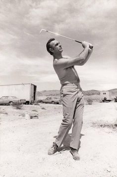 a man swinging a golf club on top of a dirt field